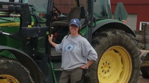 En kvinna i keps står framför en traktor